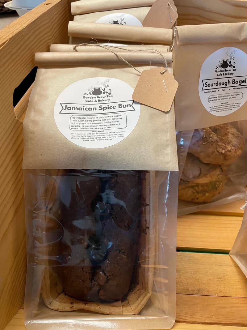 A dark Jamaican spice bun in a kraft-paper bag with a Garden Brew Tea Cafe & Bakery label